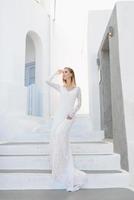 o lindo cabelo loiro jovem noiva azul em um vestido longo sexy branco de casamento em santorini na grécia foto