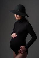 jovem e bela mulher grávida em body preto e chapéu.