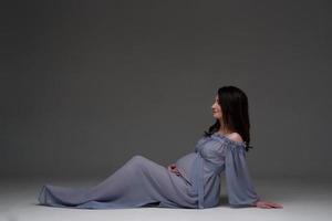 uma jovem grávida de vestido fica em um fundo cinza. foto