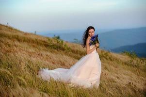 a noiva em um lindo vestido azul com um decote profundo nas costas com uma coroa de flores brancas na cabeça fica em um fundo de montanhas e lagos foto
