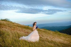 a noiva em um lindo vestido azul com um decote profundo nas costas com uma coroa de flores brancas na cabeça fica em um fundo de montanhas e lagos foto