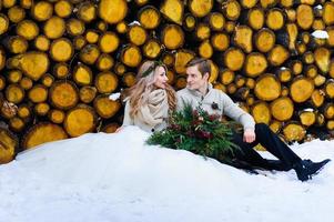 noivo beija sua noiva no templo. recém-casados com buquê senta-se na neve no fundo de madeira. casamento de inverno foto