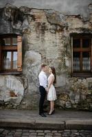 casal apaixonado está beijando e abraçando sobre o muro urbano cinza na cidade de manhã. homem e mulher estão se divertindo muito juntos. antiga antiga rua da cidade europeia com paredes de pedra. foto