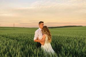 noivos em um campo de trigo. o casal se abraça durante o pôr do sol foto