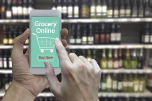 mão use smartphone com mercearia on-line na tela sobre supermercado turva e loja de varejo no fundo interior do shopping foto