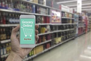 mão use smartphone com mercearia on-line na tela sobre supermercado turva e loja de varejo no fundo interior do shopping