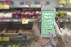 mão use smartphone com mercearia on-line na tela sobre supermercado turva e loja de varejo no fundo interior do shopping