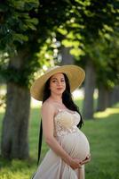 mulher grávida de chapéu posando em um vestido em um fundo de árvores verdes. foto