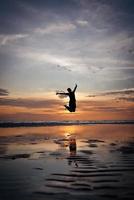 silhueta de homem pulando na praia ao pôr do sol foto