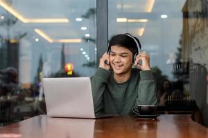 estudante universitário masculino asiático estudando on-line usando um laptop no café ou cafeteria foto