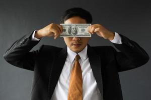 empresário ganancioso de terno cobrindo os olhos com notas de dólar. conceito de corrupção e suborno foto