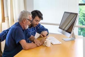 jovem ou filho ensinando seu avô pai idoso aprendendo a usar o computador em casa. foto