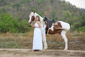 jovem e bonita com seu cavalo na luz do sol à noite. fotografia ao ar livre com garota modelo de moda. humor de estilo de vida foto