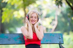 linda mulher loira em pé enquanto ouve música no fone de ouvido no parque. foto