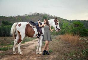 jovem e bonita com seu cavalo na luz do sol à noite. fotografia ao ar livre com garota modelo de moda. humor de estilo de vida foto