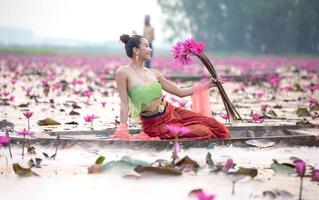 jovens mulheres asiáticas em trajes tradicionais no barco e flores de lótus rosa na lagoa foto