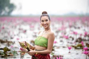 jovens mulheres asiáticas em trajes tradicionais no barco e flores de lótus rosa na lagoa foto