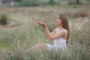 bela jovem sentada no campo na grama verde e soprando dente de leão. ao ar livre. Aproveite a natureza. menina sorridente saudável no gramado da primavera. conceito livre de alergia. liberdade foto