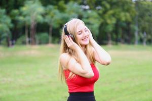 linda mulher loira em pé enquanto ouve música no fone de ouvido no parque. foto