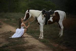 jovem e bonita com seu cavalo na luz do sol à noite. fotografia ao ar livre com garota modelo de moda. humor de estilo de vida foto