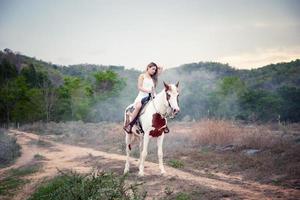 jovem e bonita com seu cavalo na luz do sol à noite. fotografia ao ar livre com garota modelo de moda. humor de estilo de vida foto