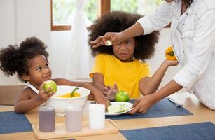 feliz família multinacional de raça mista com filhas preparar salada fresca orgânica vegetal, desfrutar do processo de cozimento do passatempo na cozinha aconchegante, alimentação saudável, pais ensinam crianças, atividade de fim de semana em casa foto