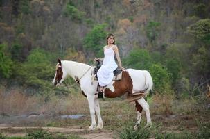 jovem e bonita com seu cavalo na luz do sol à noite. fotografia ao ar livre com garota modelo de moda. humor de estilo de vida foto