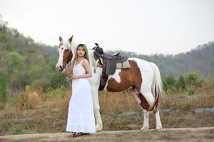 jovem e bonita com seu cavalo na luz do sol à noite. fotografia ao ar livre com garota modelo de moda. humor de estilo de vida foto