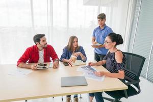 grupo diversificado de jovens empresários discutindo um projeto de trabalho enquanto estão sentados juntos em uma mesa em um escritório moderno. conceito de coworking foto