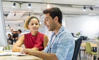 diversos colegas de trabalho sentados em uma mesa em um escritório moderno conversando em um computador. foto