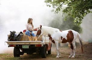 jovem e bonita com seu cavalo na luz do sol à noite. fotografia ao ar livre com garota modelo de moda. humor de estilo de vida foto