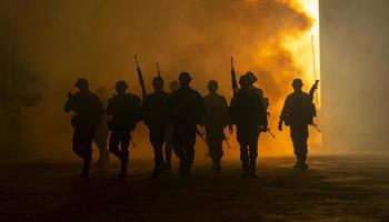 silhuetas de soldados do exército no nevoeiro contra um pôr do sol, equipe de fuzileiros navais em ação, cercado de fogo e fumaça, atirando com rifle de assalto e metralhadora, atacando inimigo