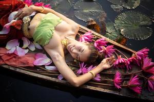 jovens mulheres asiáticas em trajes tradicionais no barco e flores de lótus rosa na lagoa foto