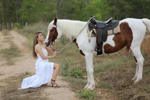 jovem e bonita com seu cavalo na luz do sol à noite. fotografia ao ar livre com garota modelo de moda. humor de estilo de vida foto