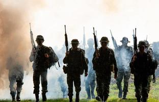 silhuetas de soldados do exército no nevoeiro contra um pôr do sol, equipe de fuzileiros navais em ação, cercado de fogo e fumaça, atirando com rifle de assalto e metralhadora, atacando inimigo