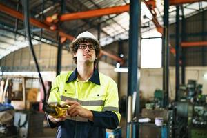 engenheiro industrial ou trabalhador usando um capacete em pé em uma fábrica industrial pesada. a manutenção procurando trabalhar em máquinas industriais e verificar a configuração do sistema de segurança na fábrica. foto