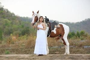 jovem e bonita com seu cavalo na luz do sol à noite. fotografia ao ar livre com garota modelo de moda. humor de estilo de vida foto