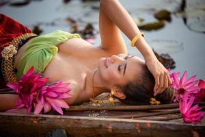 jovens mulheres asiáticas em trajes tradicionais no barco e flores de lótus rosa na lagoa foto