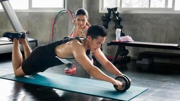 casal atleta desportista fazendo exercício com roda de rolo abs para fortalecer seu músculo abdominal no ginásio. foto