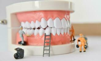 pessoas em miniatura para reparar um dente ou trabalhador de figura pequena, limpando o modelo de dente como médico e de saúde. foto