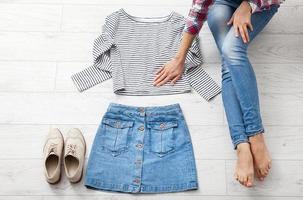 roupa casual de verão com diferentes acessórios e pernas femininas em jeans no piso de madeira branco. vista superior e copie o espaço. foto