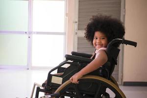 Africano - etnia americana menina descansando na cadeira de rodas enquanto espera para ver o médico no hospital. africano - garota americana sentada em uma cadeira de rodas e sorrindo para a câmera. foto
