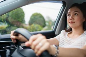 motorista do sexo feminino irreconhecível usando a mão esquerda agarra no volante enquanto dirige na estrada, mulher dirigindo um carro elétrico moderno ev na bela luz do sol na estrada. conceito de condução de segurança. foto