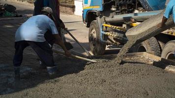 grupo de trabalhadores da construção civil asiáticos com caminhão betoneira estão despejando concreto no chão no canteiro de obras foto