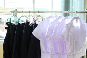 uniformes de estudantes depois de lavados pendurados no varal. camisas brancas e saias azuis secando no cabideiro dentro de casa. de volta ao conceito de escola. foto