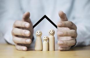 empresário duas mãos protegendo o modelo de madeira da família para o conceito de seguro e garantia de vida. foto