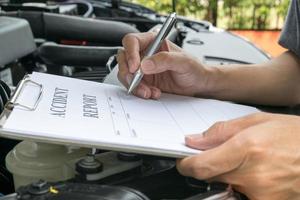 mecânico inspecionando o carro de danos e preenchendo o formulário de relatório de acidente foto