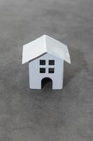 simplesmente projete com casa modelo de brinquedo branco em miniatura em fundo cinza de pedra de concreto. conceito de casa de sonho de seguro de propriedade de hipoteca. copie o espaço. foto