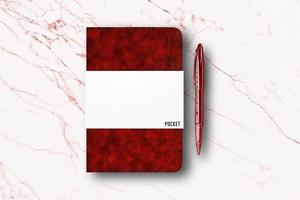 caderno de papel vermelho em branco ou livro de bolso e uma caneta no fundo da mesa de mármore branco. foto
