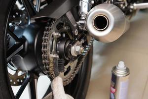 mecânico usando escova de latão limpa e mantém a corrente e as rodas dentadas da motocicleta, manutenção, reparação do conceito de motocicleta na garagem. foco seletivo foto